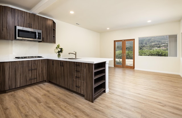 kitchen featuring kitchen peninsula, dark brown cabinetry, light wood-type flooring, and sink