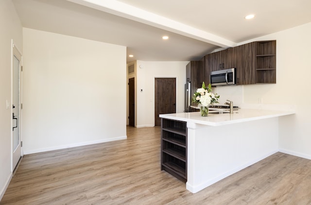 kitchen with sink, dark brown cabinetry, appliances with stainless steel finishes, light hardwood / wood-style floors, and kitchen peninsula