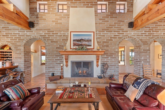 living room with beamed ceiling, light tile patterned flooring, a towering ceiling, and brick wall