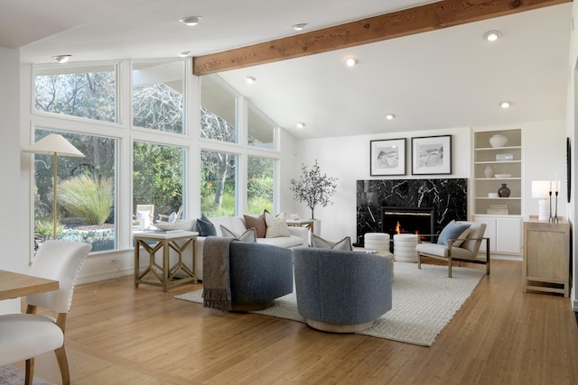 living room featuring beam ceiling, light wood-style flooring, a premium fireplace, high vaulted ceiling, and baseboards