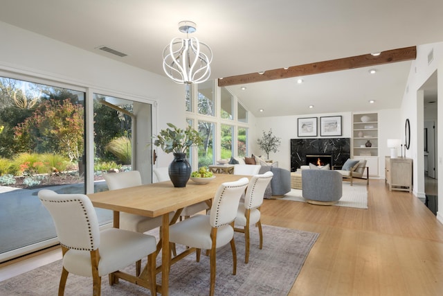 dining space with lofted ceiling with beams, a notable chandelier, a premium fireplace, visible vents, and light wood-type flooring