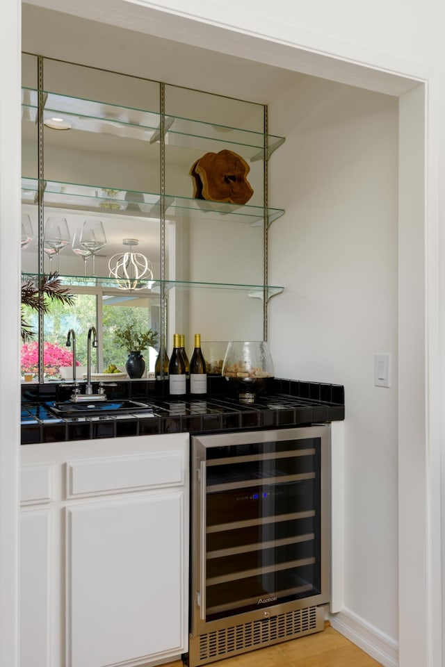 bar with wine cooler, light wood-style flooring, a sink, wet bar, and baseboards