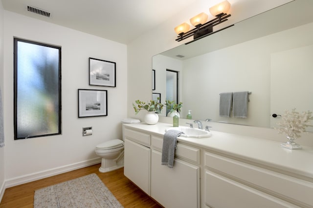 bathroom featuring visible vents, toilet, vanity, wood finished floors, and baseboards