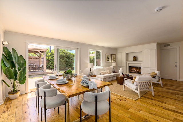 dining room with ornamental molding, visible vents, light wood finished floors, and a lit fireplace