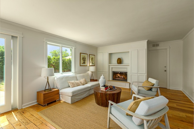 living area featuring light wood finished floors, a glass covered fireplace, visible vents, and ornamental molding