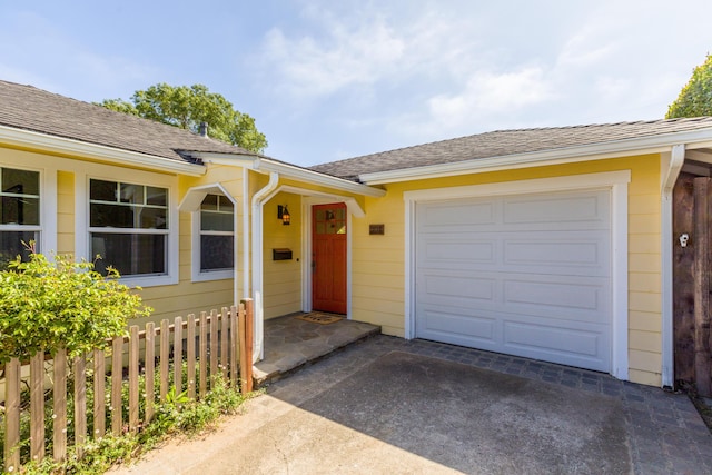 property entrance featuring an attached garage, driveway, fence, and roof with shingles