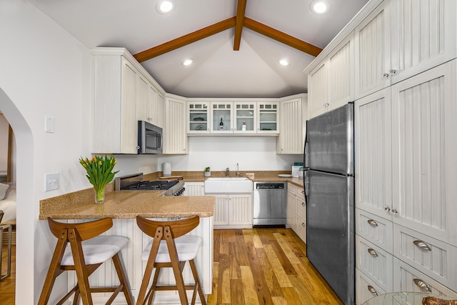 kitchen with lofted ceiling with beams, light wood-style floors, arched walkways, stainless steel appliances, and a peninsula