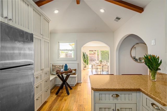kitchen with light stone counters, lofted ceiling with beams, light wood-style floors, visible vents, and freestanding refrigerator