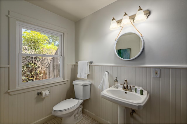bathroom with a sink, toilet, wainscoting, baseboards, and tile patterned flooring