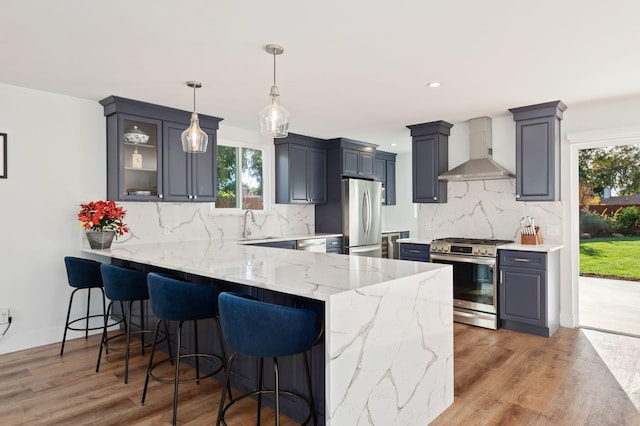 kitchen featuring wall chimney range hood, pendant lighting, kitchen peninsula, hardwood / wood-style flooring, and appliances with stainless steel finishes