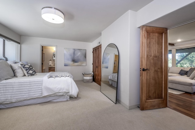 bedroom featuring baseboards, ensuite bathroom, and light colored carpet