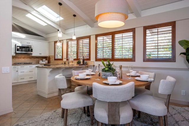 dining space featuring light tile patterned floors, vaulted ceiling with skylight, and baseboards