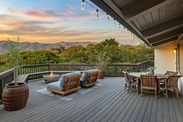 deck at dusk featuring an outdoor fire pit, outdoor dining area, and a mountain view