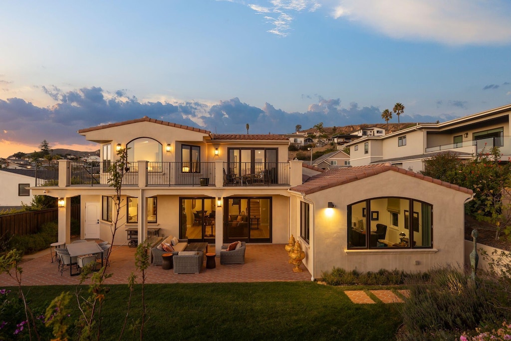 back house at dusk featuring a yard, a patio area, an outdoor living space, and a balcony