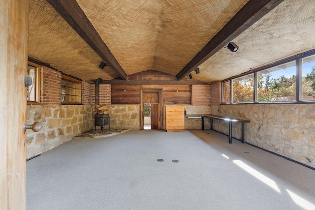 unfurnished living room with carpet flooring, a wood stove, and vaulted ceiling with beams