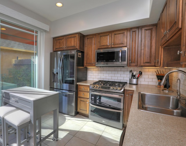 kitchen with brown cabinetry, decorative backsplash, stainless steel appliances, light countertops, and a sink