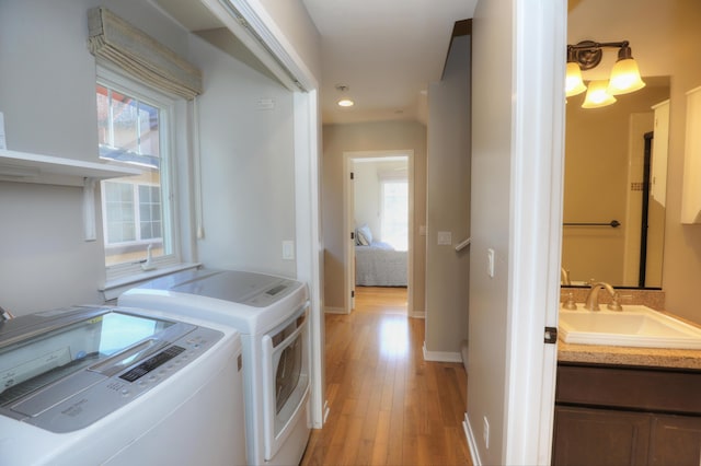 laundry room with laundry area, light wood finished floors, baseboards, washer and clothes dryer, and a sink