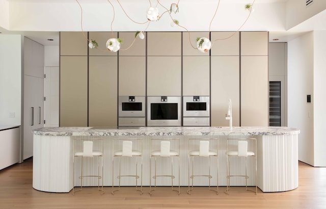 kitchen featuring light hardwood / wood-style floors, wall oven, oven, light stone counters, and a center island