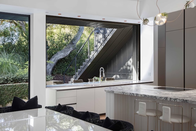 kitchen featuring decorative light fixtures, white cabinets, light stone countertops, and a wealth of natural light