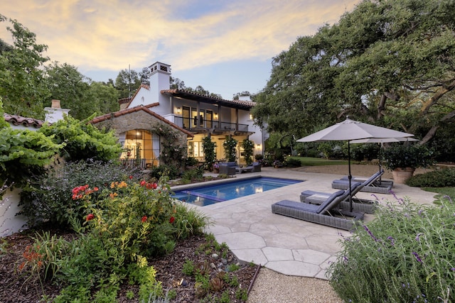 pool at dusk featuring a jacuzzi and a patio