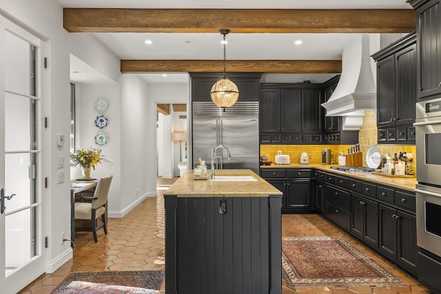 kitchen with hanging light fixtures, backsplash, a kitchen island with sink, appliances with stainless steel finishes, and custom exhaust hood