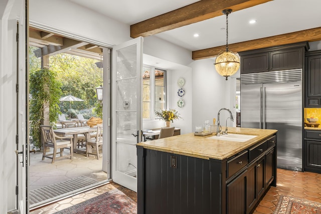 kitchen featuring a kitchen island with sink, sink, hanging light fixtures, built in refrigerator, and beamed ceiling