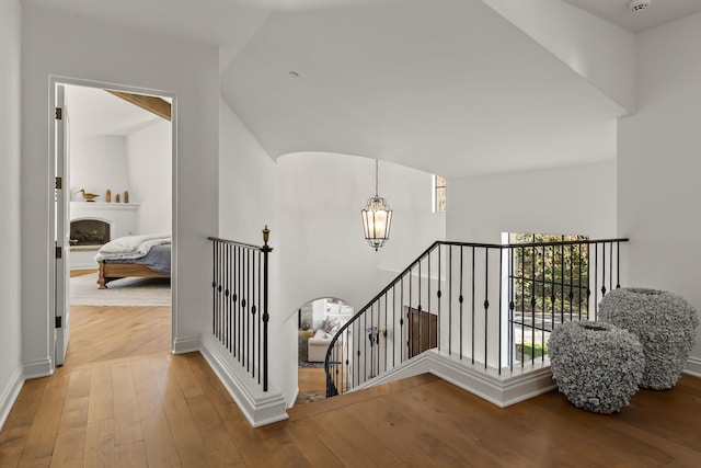 stairs featuring a large fireplace, wood-type flooring, and an inviting chandelier