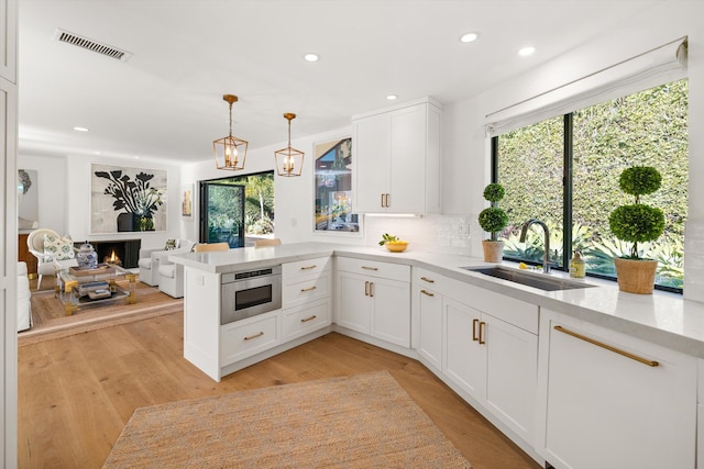 kitchen featuring white cabinets, kitchen peninsula, pendant lighting, stainless steel microwave, and sink