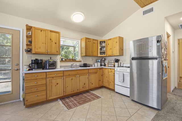 kitchen featuring sink, white gas range oven, vaulted ceiling, stainless steel fridge, and light tile patterned floors