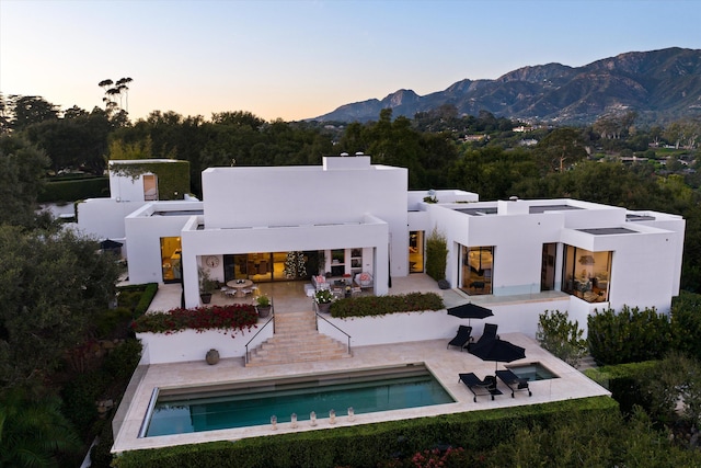 back house at dusk with a patio area, a mountain view, and an outdoor living space