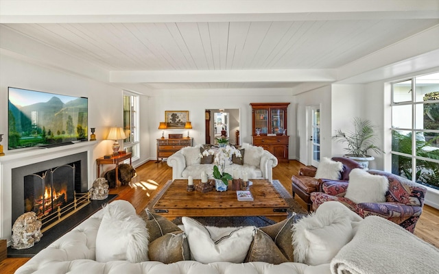 living room with a warm lit fireplace, light wood-style flooring, and beamed ceiling