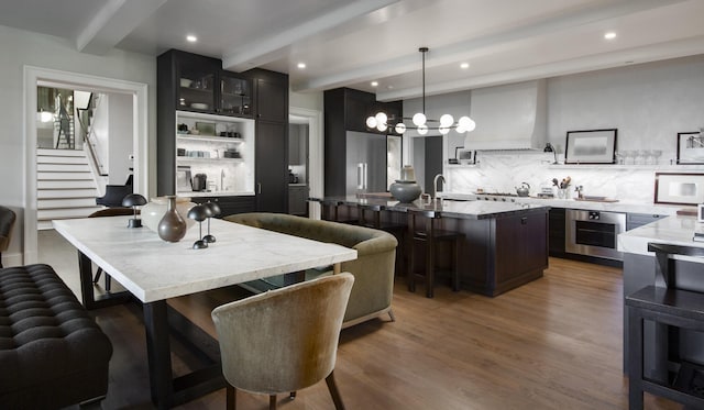 kitchen featuring wall chimney range hood, an island with sink, a kitchen bar, decorative light fixtures, and oven