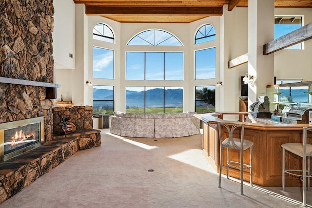 carpeted living room featuring a high ceiling, beamed ceiling, a mountain view, indoor bar, and a fireplace