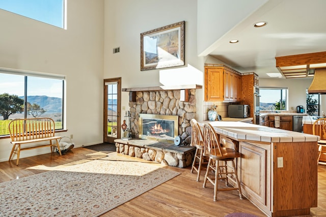 kitchen with kitchen peninsula, a kitchen breakfast bar, stainless steel dishwasher, a fireplace, and tile counters