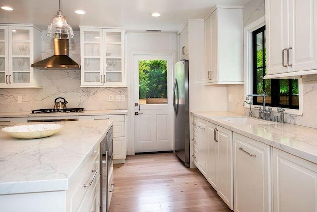 kitchen featuring white cabinets, sink, wall chimney exhaust hood, and decorative light fixtures