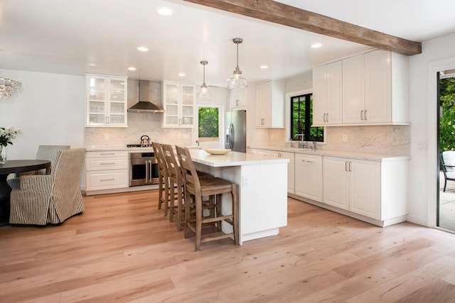 kitchen with white cabinets, beam ceiling, stainless steel appliances, and wall chimney exhaust hood