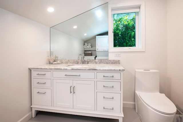 bathroom with stacked washer and dryer, vanity, lofted ceiling, and toilet