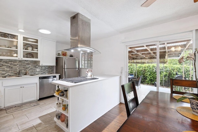 kitchen featuring island exhaust hood, appliances with stainless steel finishes, tasteful backsplash, sink, and white cabinetry