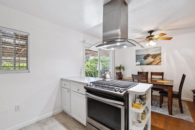 kitchen featuring gas range, a textured ceiling, island range hood, ceiling fan, and white cabinetry