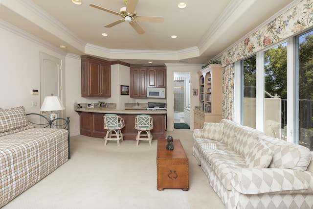 living room featuring ceiling fan, light carpet, a tray ceiling, and ornamental molding