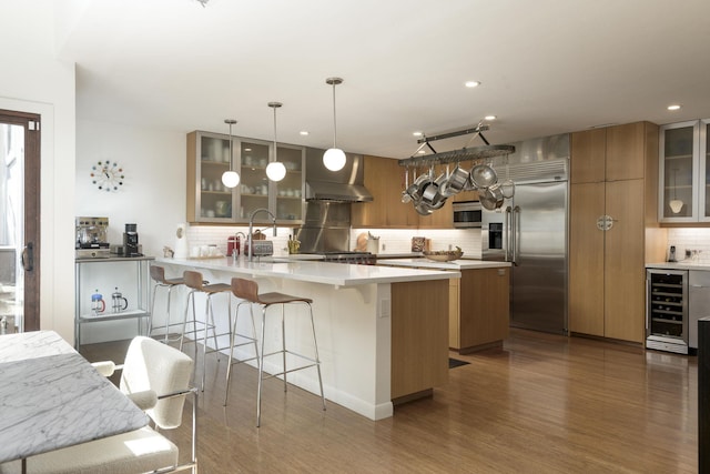 kitchen with wall chimney exhaust hood, a breakfast bar, hanging light fixtures, appliances with stainless steel finishes, and beverage cooler