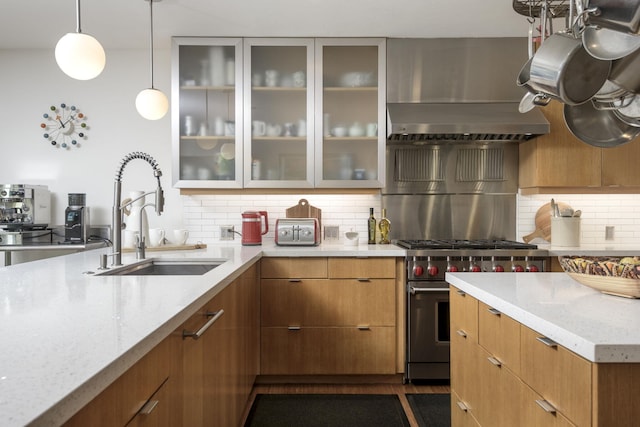 kitchen with sink, backsplash, hanging light fixtures, light stone counters, and high end stove