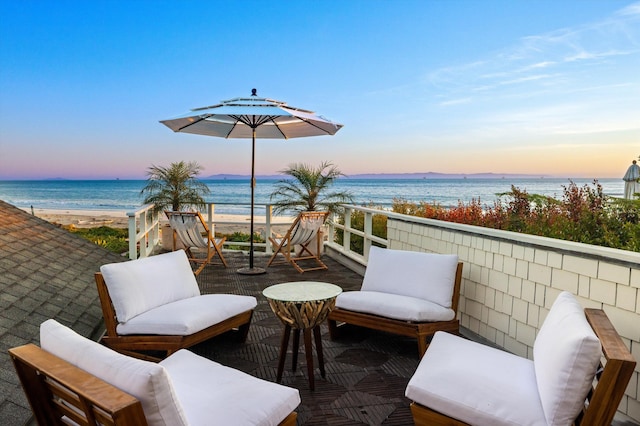 patio terrace at dusk featuring a view of the beach, a water view, and a balcony