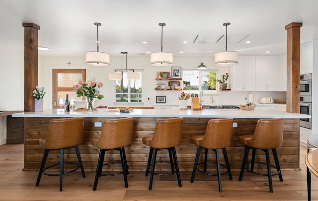 kitchen with white cabinets, a kitchen breakfast bar, hanging light fixtures, and light hardwood / wood-style flooring