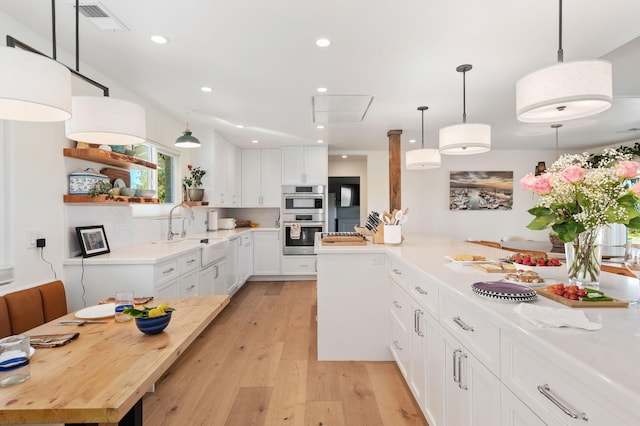 kitchen featuring pendant lighting, sink, stainless steel double oven, light wood-type flooring, and white cabinetry