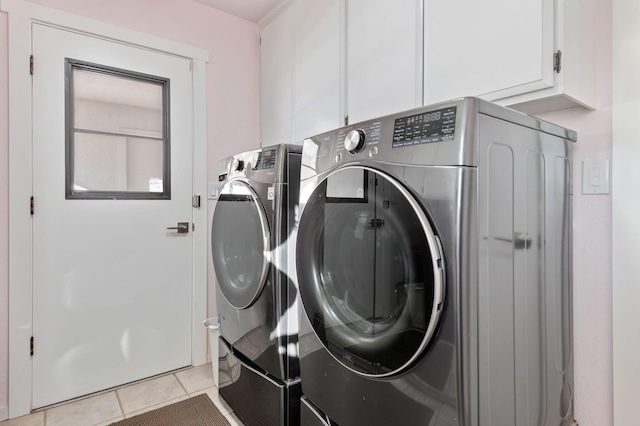 clothes washing area featuring cabinets, washing machine and dryer, and light tile patterned floors