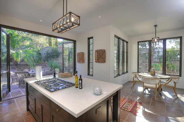 kitchen with a center island, decorative light fixtures, dark tile patterned flooring, and stainless steel gas stovetop