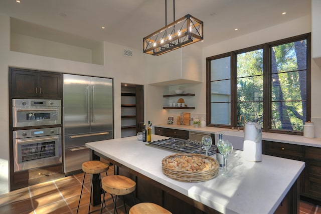 kitchen featuring tile patterned flooring, appliances with stainless steel finishes, decorative light fixtures, a kitchen island, and a kitchen bar