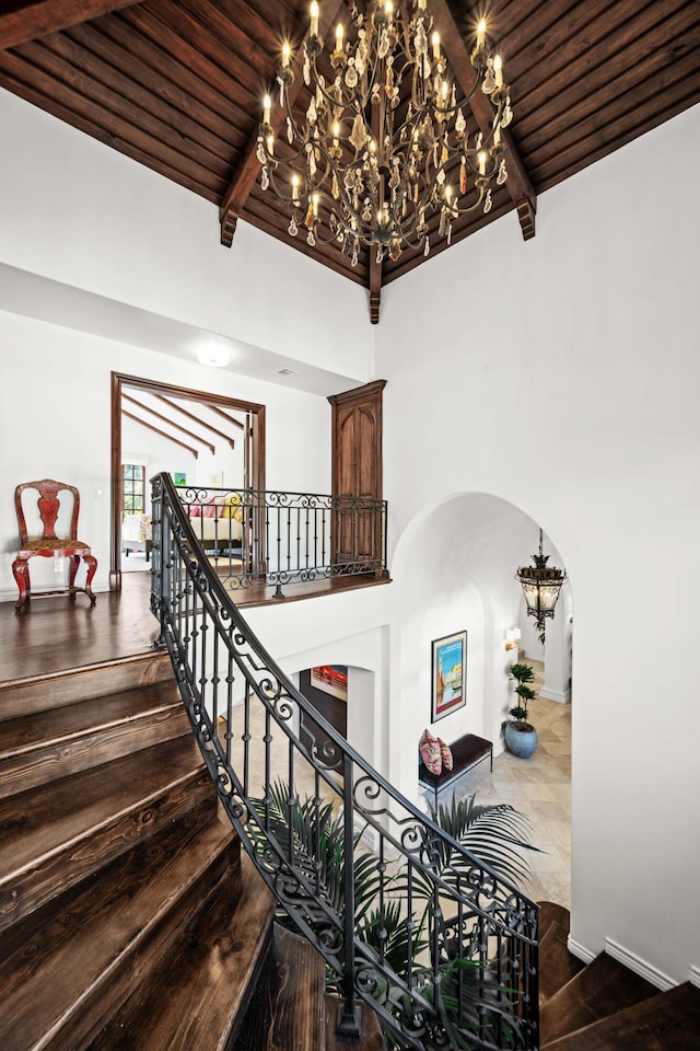 staircase featuring beam ceiling, a towering ceiling, a notable chandelier, and wood ceiling