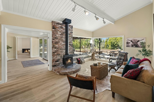 living room with a wood stove, vaulted ceiling with beams, track lighting, and light wood-type flooring